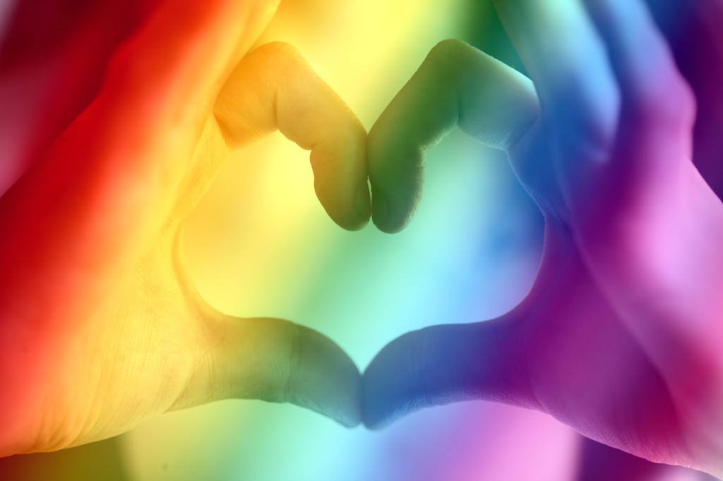 rich rainbow-colored background with hands creating a heart