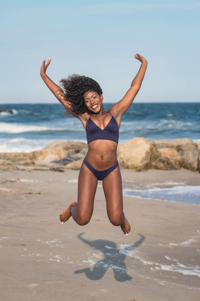 happy black lady in a blue bikini jumping up on the beach