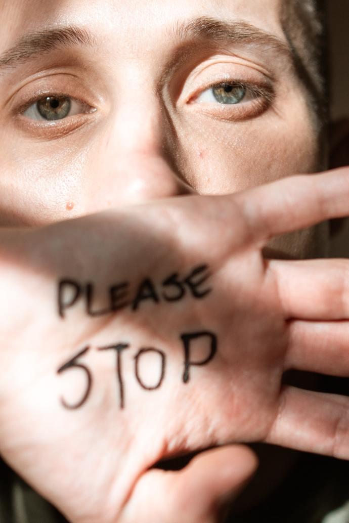 woman holding up one hand with her palm showing in front of her face that says "Please Stop"