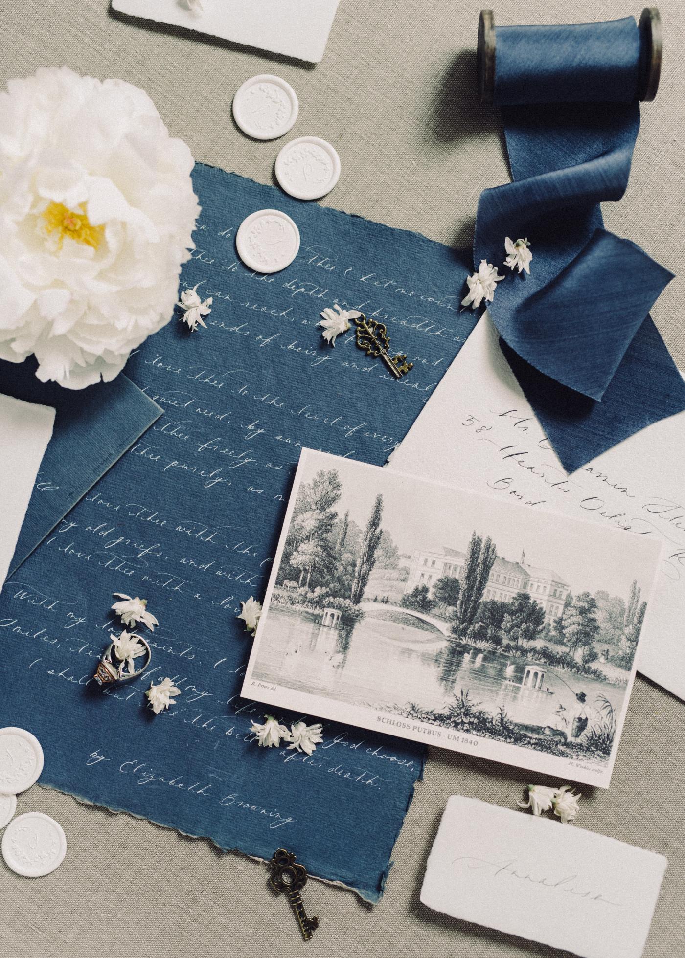 Scrapbooking items. White buttons, blue paper with a handwritten letter, black and white photograph, a spool of blue ribbon and a white carnation