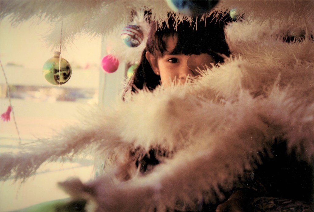 little girl with a patch on her right eye standing behind white Christmas tree branches 