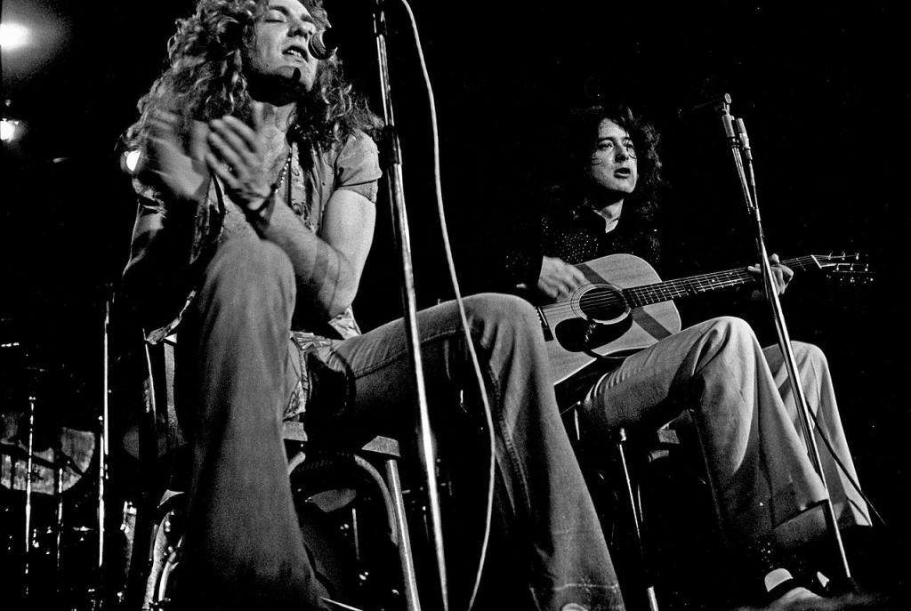 Black and white of Robert Plant and Jimmy Page of Led Zeppelin in 1979 sitting down singing and in concert.
