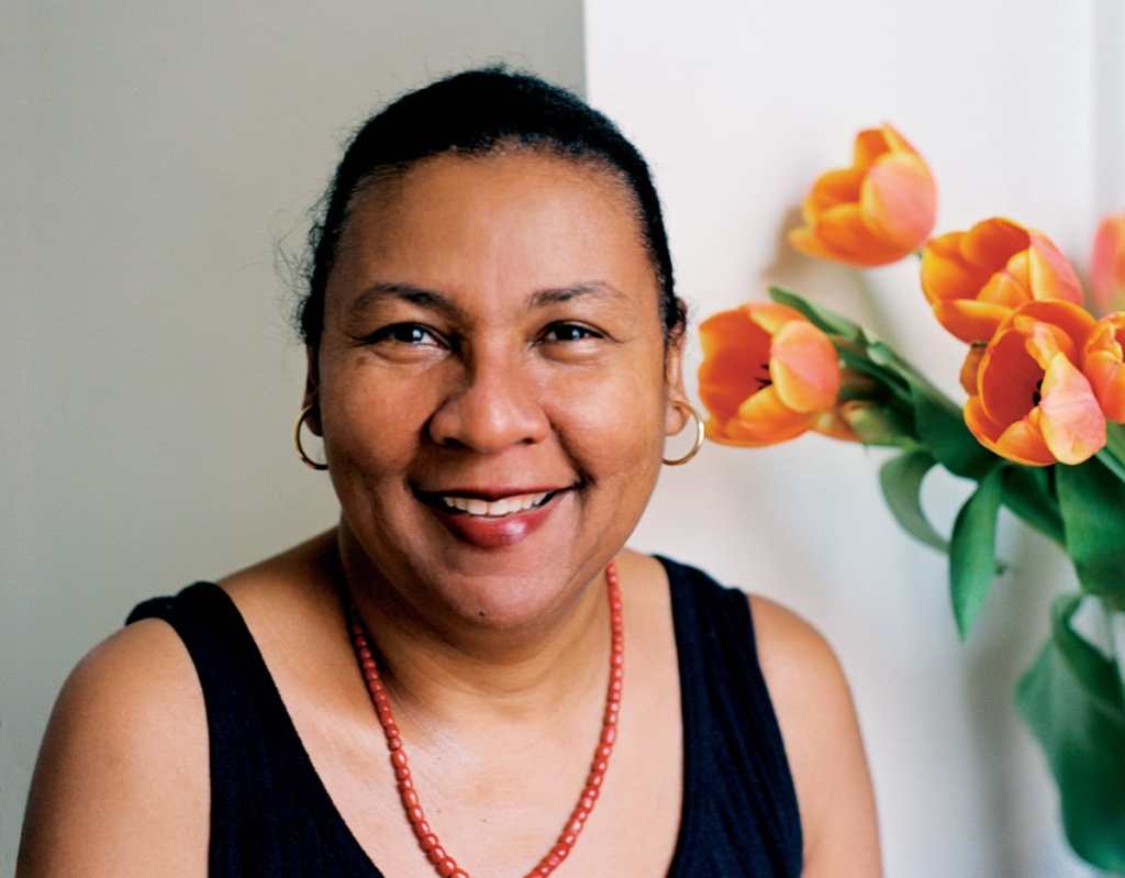 bell hooks head shot, smiling in a black tank top with orange beads and orange tulips toward the upper right, book review of The Will to Change 