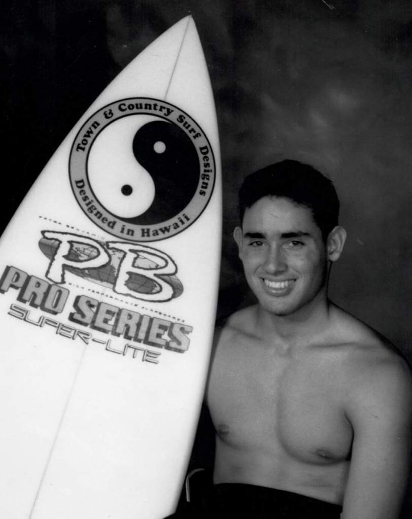 Surfer "Dito" posing shirtless with his Pro Series surfboard
