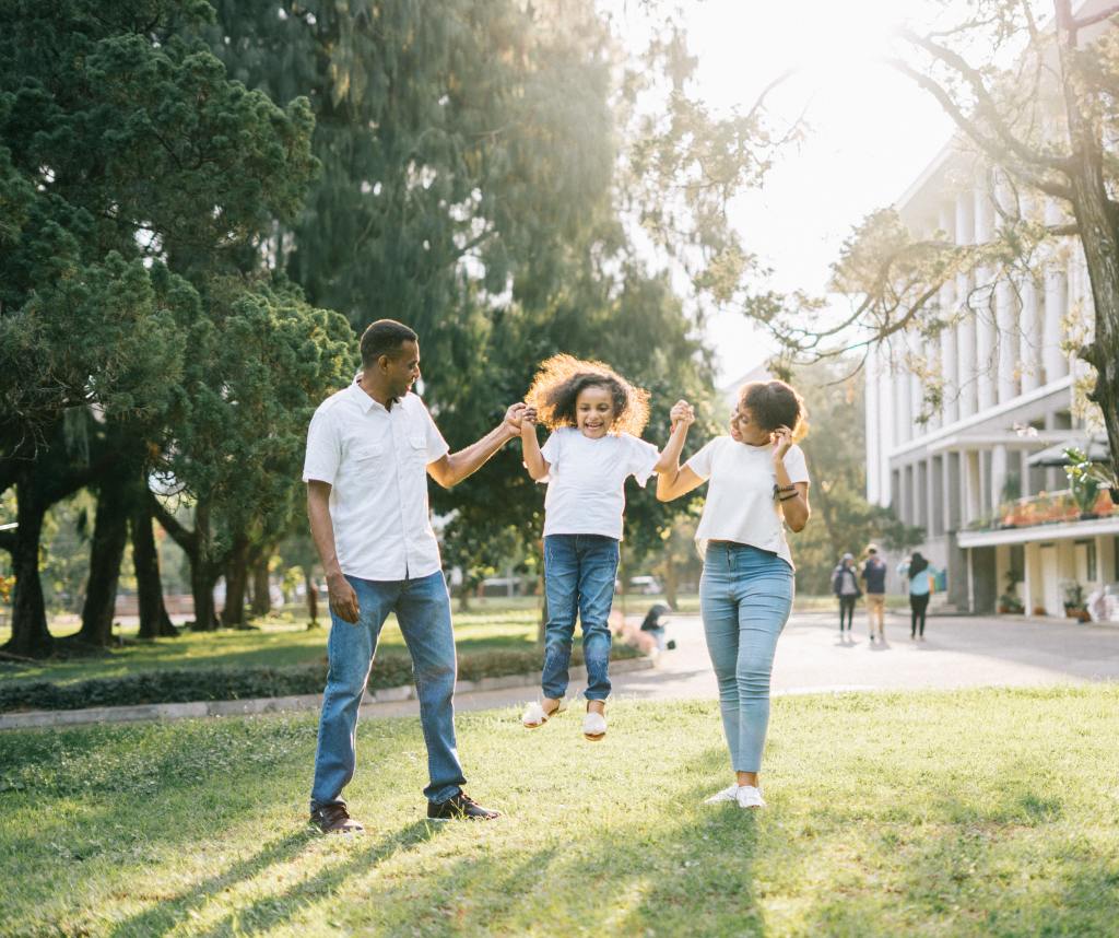 Man, woman, and girl at a park with the man and woman lifting the girl off the ground 
