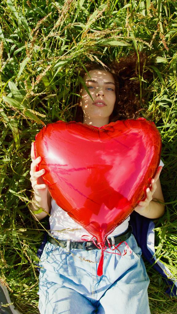 girl laying on grass holding a large balloon heart