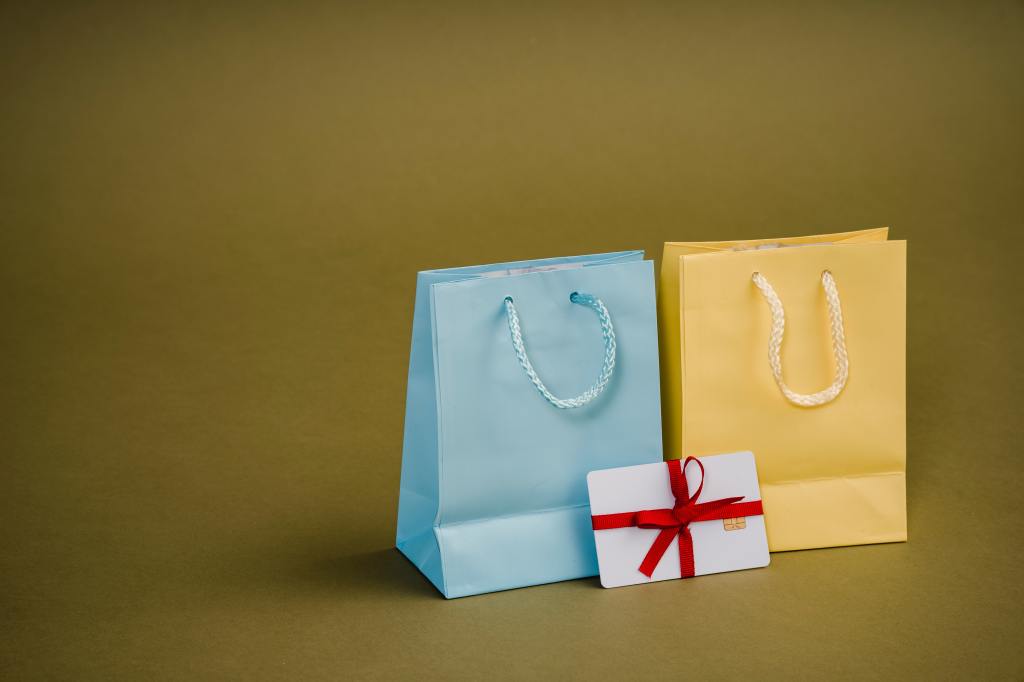 Two gift bags: one light blue and one yellow and a note in a red bow with them. 