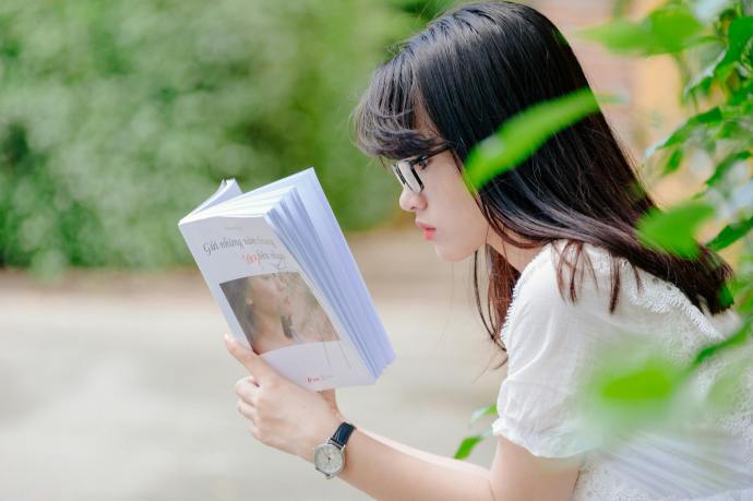 young woman outside sitting with book in hand reading