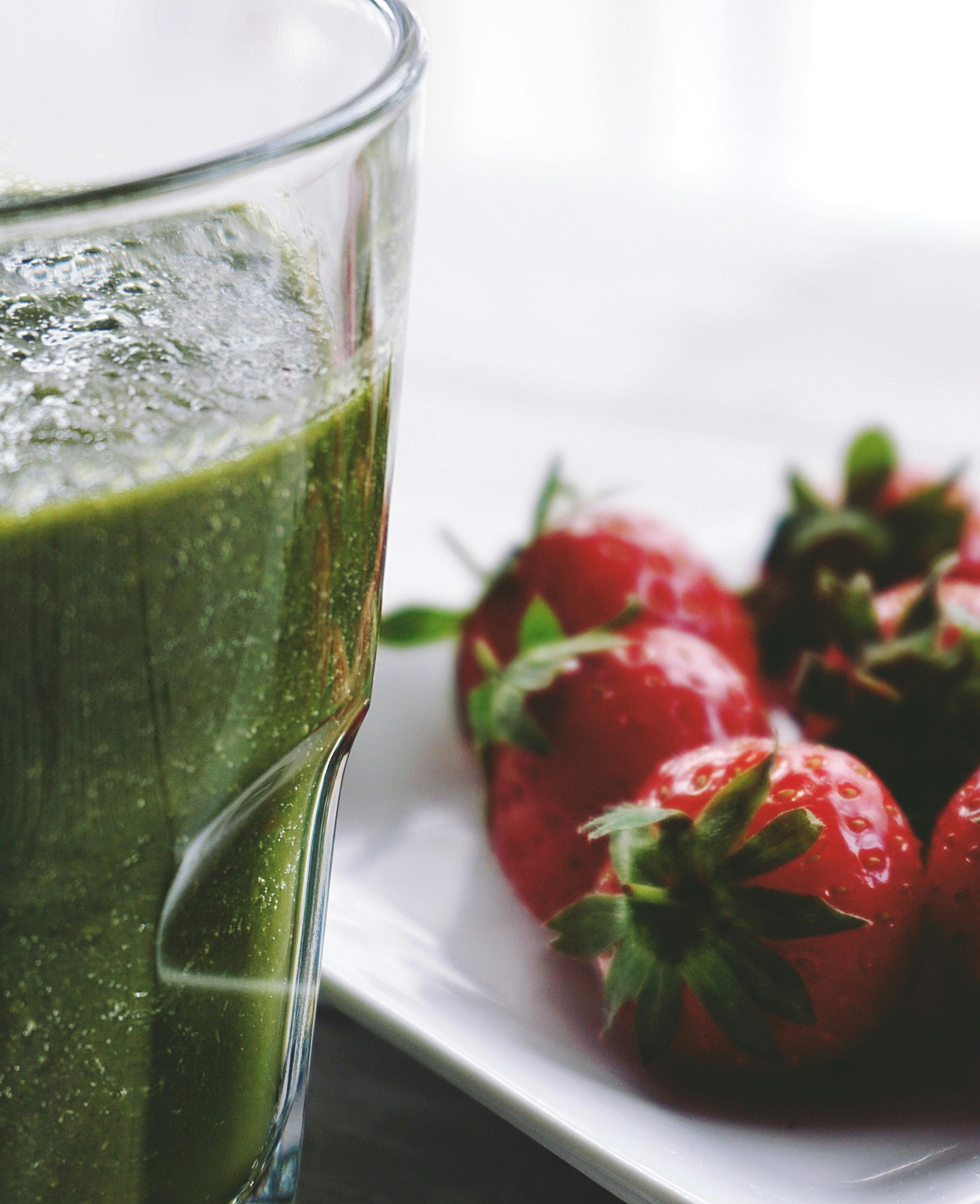 green smoothie glass with strawberries to the side